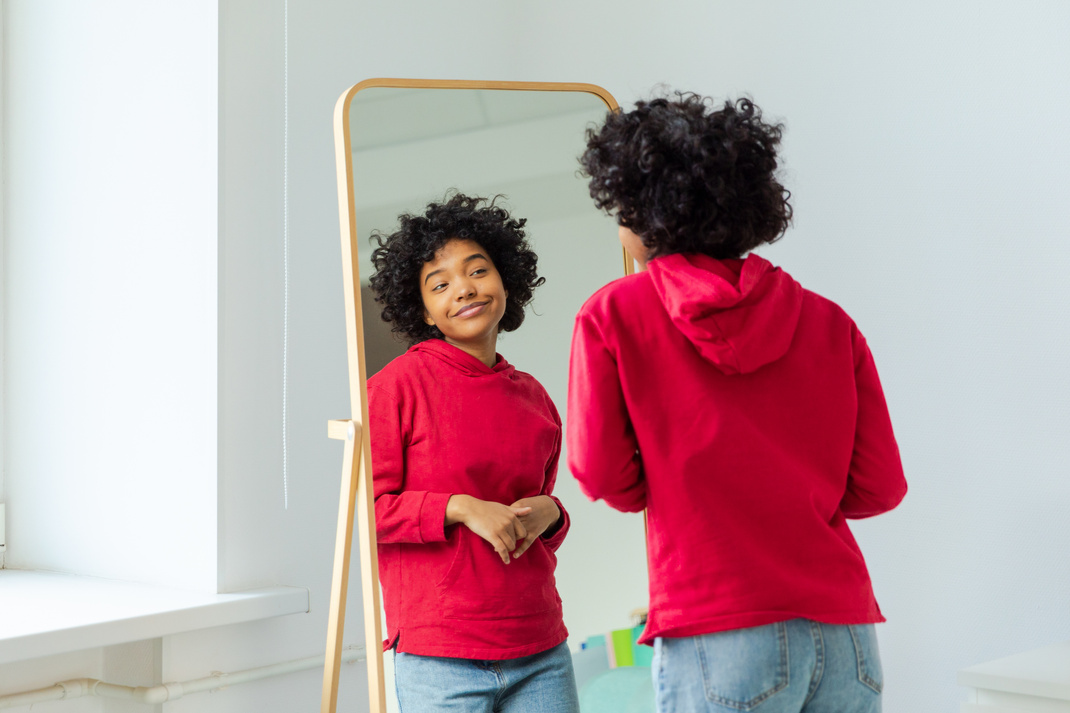 Love yourself. Beautiful young smiling african american woman dancing enjoying her mirror reflection. Black lady looking at mirror looking confident and happy. Self love concept.
